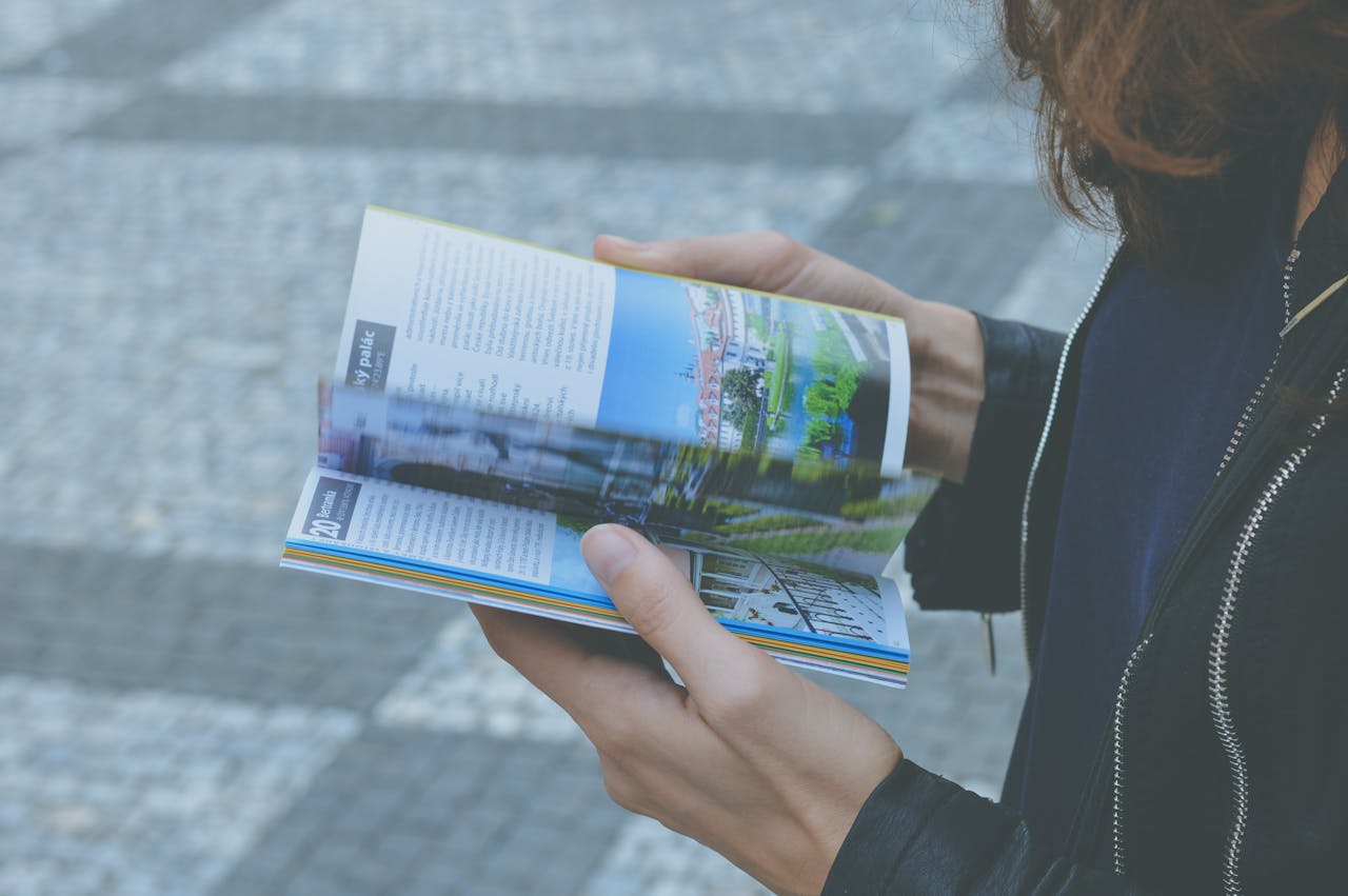 services-01 A person flipping through a travel book outdoors, showcasing a variety of vibrant pages.