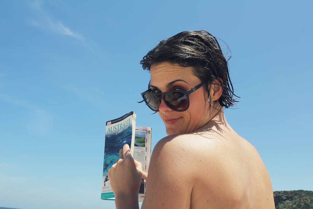 why-choose-us Woman with sunglasses reading a travel guide on a sunny Australian beach.