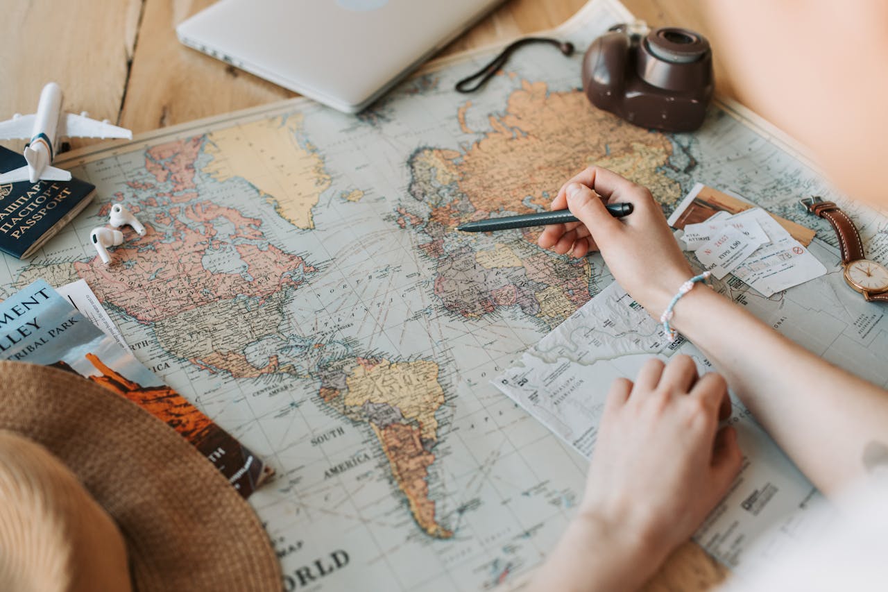 journey Hands marking destinations on a world map surrounded by travel essentials like passport and camera.